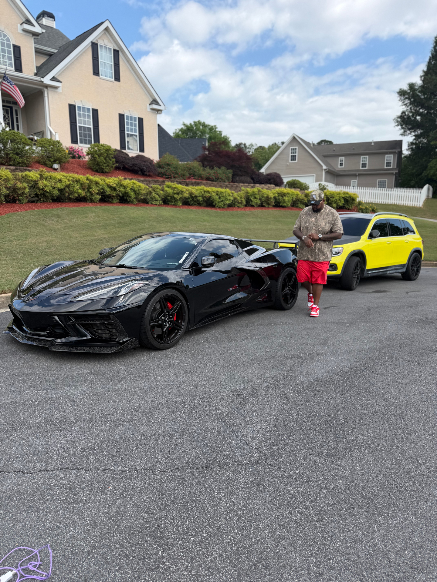 Bruce Webb with his black Corvette and yellow Mercedes GLB in the driveway
